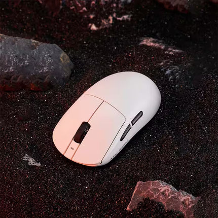 A white wireless gaming mouse with black scroll and side buttons, resting on a dark textured surface with rocks.