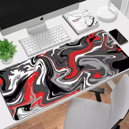 A large rectangular desk mat with a black, white, and red liquid marble swirl pattern, shown on a white desk next to an Apple iMac, keyboard, plant, and phone.