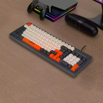 Mechanical keyboard with orange and black keys on a wooden surface, with gaming console and accessories in the background.
