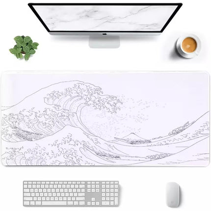 A large rectangular desk mat featuring a black line art print of a classic ocean wave, styled on a white desk with an iMac, keyboard, mouse, and a small plant.