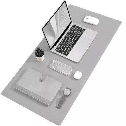 A gray desk mat with a laptop, mouse, notebook, small plant, and watch arranged on top, shown from an overhead angle on a white background.