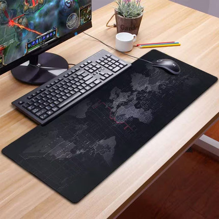 Desk setup with a world map mouse pad, keyboard, and monitor on a wooden desk.