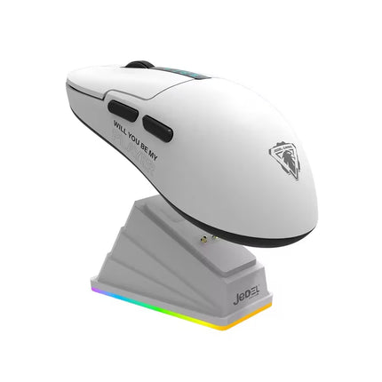 A white ergonomic gaming mouse with black buttons and a silver logo, resting on a gray charging dock with RGB lighting, on a white background.