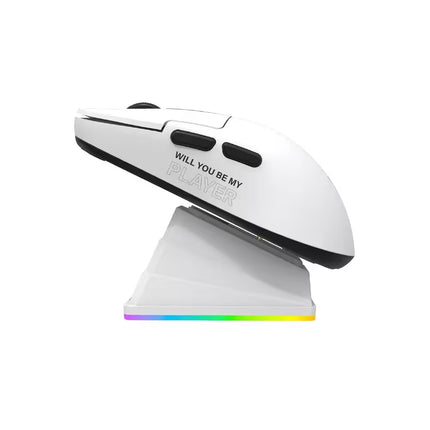 A white wireless gaming mouse with black accents and the text 'WILL YOU BE MY PLAYER' printed on the side, resting on a matching white charging dock that has a colorful RGB light strip.