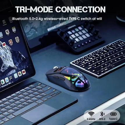 A wireless gaming mouse with a glossy black body and vibrant RGB rainbow lighting, shown on a dark desk next to a laptop, keyboard, and audio controller. Text overlays highlight its tri-mode connection and Bluetooth 5.
